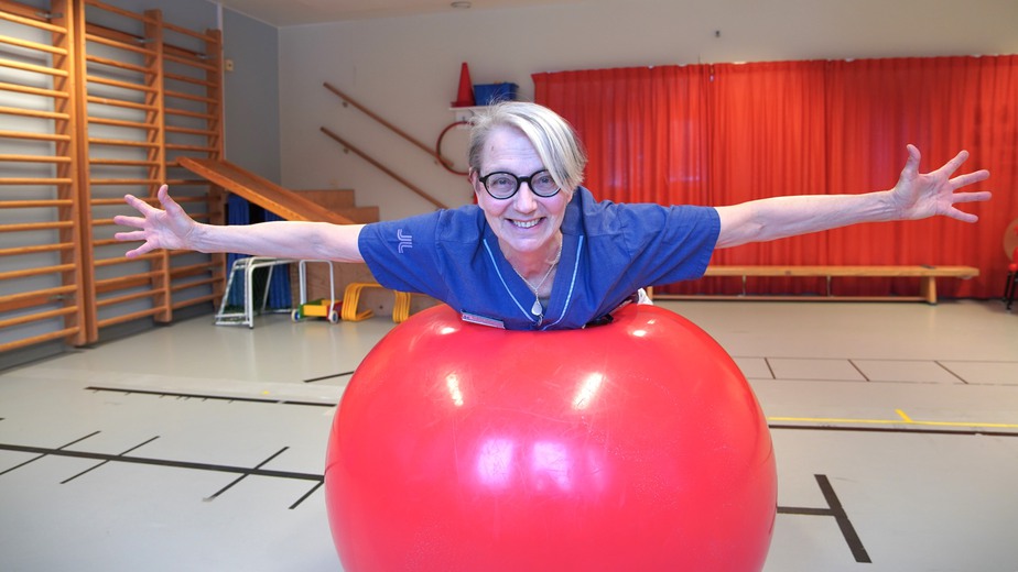 Birgitta ligger över en stor röda pilatesboll med båda armarna utsträckta åt sidan.