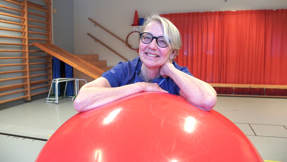 Birgitta lutar sig med axeln mot en stor röd pilatesboll.