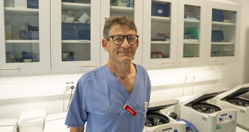 Jeffrey Yachnin står i blåa sjukhuskläder och svarta glasögon i ett forskningsrum