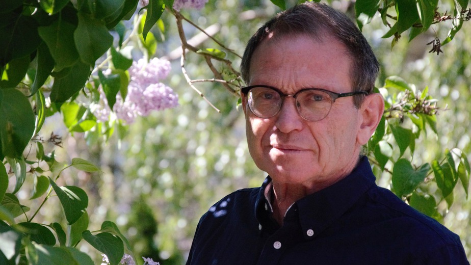 Lars Bergström står iklädd mörkblå skjorta framför en syrenbuske.