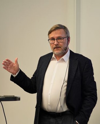 Mattias von Beckerath i vit skjorta och svart kavaj gestikulerar med vänster hand när han pratar