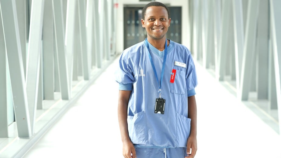 Japhet Nthezamizero med röd läkarskylt och klädd i Region Stockholms blå arbetskläder.
